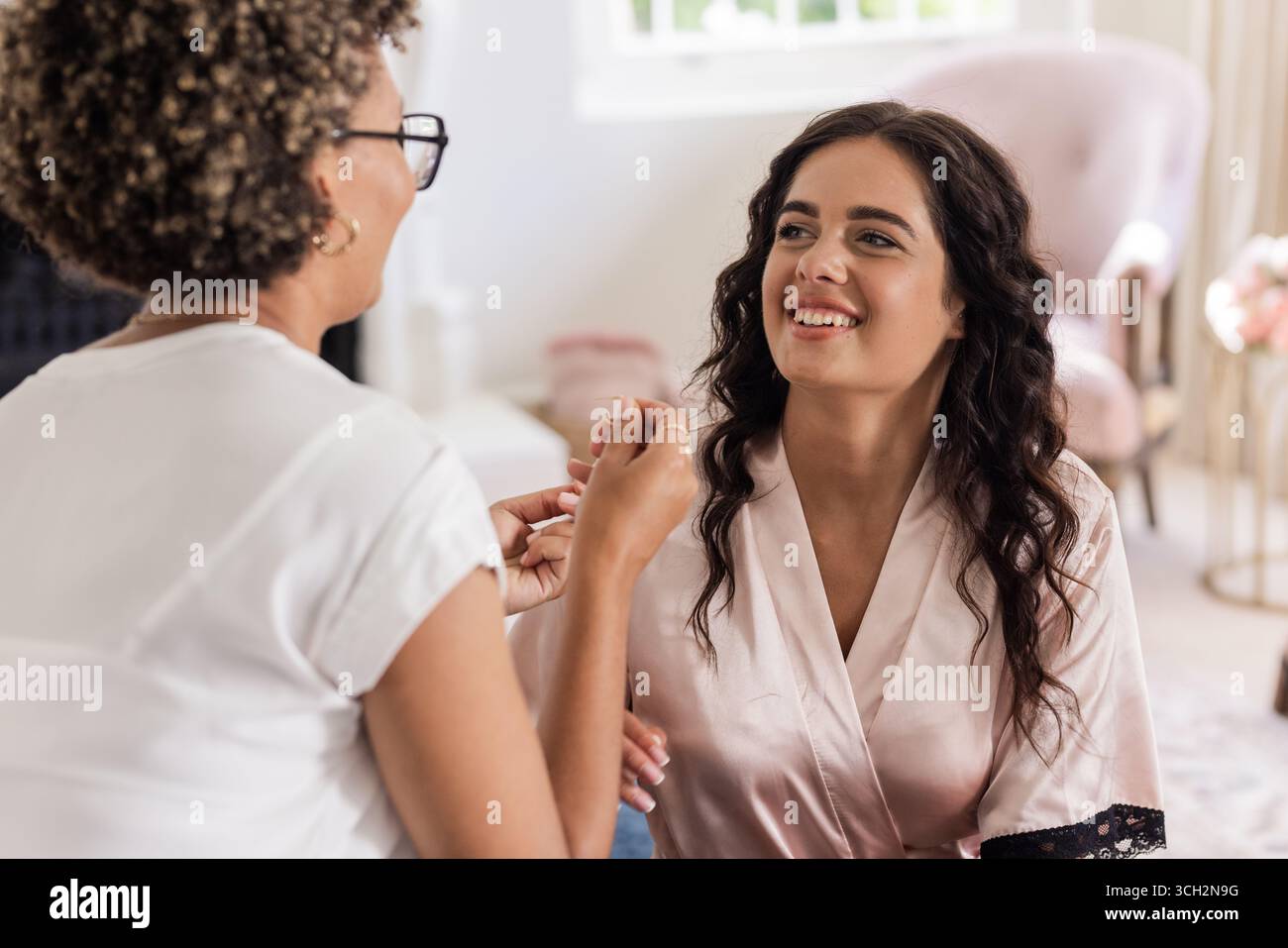 Braut macht sich fertig, lächelt, während Make-up-Künstler zu Hause den letzten Schliff anbringt Stockfoto