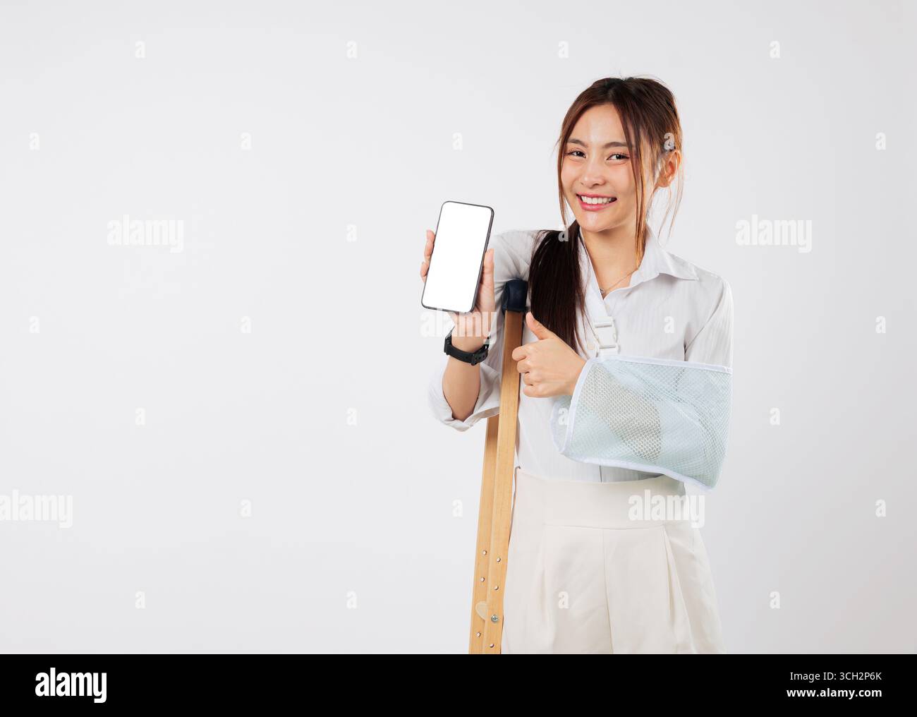 Verletzte asiatische Frau mit gebrochenem Arm, in einem Gips, das Telefon hält, benutzt mobile Unterstützung Stockfoto