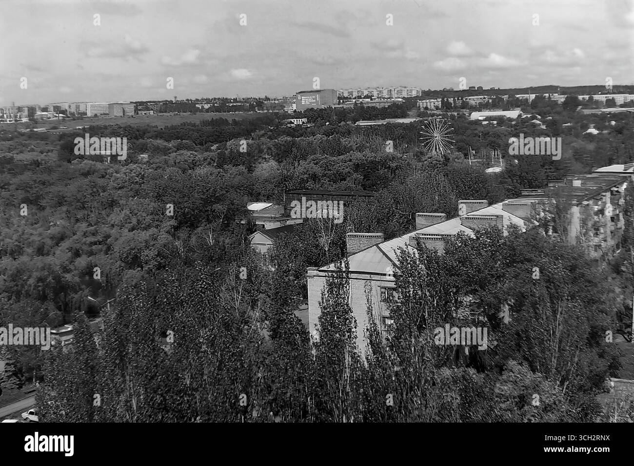 Ein fantastischer Panoramablick auf Sloviansk von einem Gebäude am Puschkin Boulevard im Juli 1997. Das Bild fängt den riesigen zentralen Park der Stadt ein, dicht mit Sommerlaub, mit dem legendären Riesenrad über den Bäumen – ein nostalgisches Symbol für die Freizeit aus der Sowjetzeit. Im Vordergrund befindet sich ein klassisches Dach aus der Stalin-Ära, und die Skyline der Stadt erstreckt sich bis in die Ferne. Dieses Archivfoto ist ein wertvolles Dokument der friedlichen, grünen Landschaft des Donbas in der postsowjetischen Ukraine und bewahrt eine Erinnerung an das alltägliche Leben lange vor dem Konflikt des 21. Jahrhunderts Stockfoto
