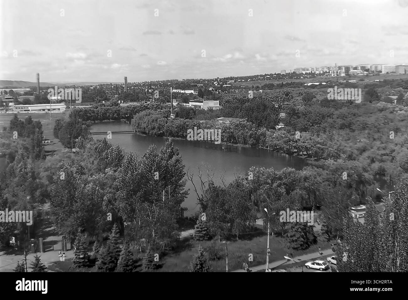 Ein Panoramablick auf einen der Salzseen (Limonen) in Sloviansk, aufgenommen an einem heißen Sommertag im Juli 1997. Der Rahmen zeigt die ruhige Wasseroberfläche umgeben von üppigem Grün, eine Fußgängerbrücke und die Skyline der Stadt am Horizont, die Wohn- und Industriebauten miteinander verbindet. Dieses Foto ist ein einzigartiges Dokument, das das Wesen einer Ferienstadt im industriellen Herzen des Donbas widerspiegelt und die Atmosphäre eines friedlichen Alltags in der postsowjetischen Ukraine vor dem Krieg einfängt Stockfoto