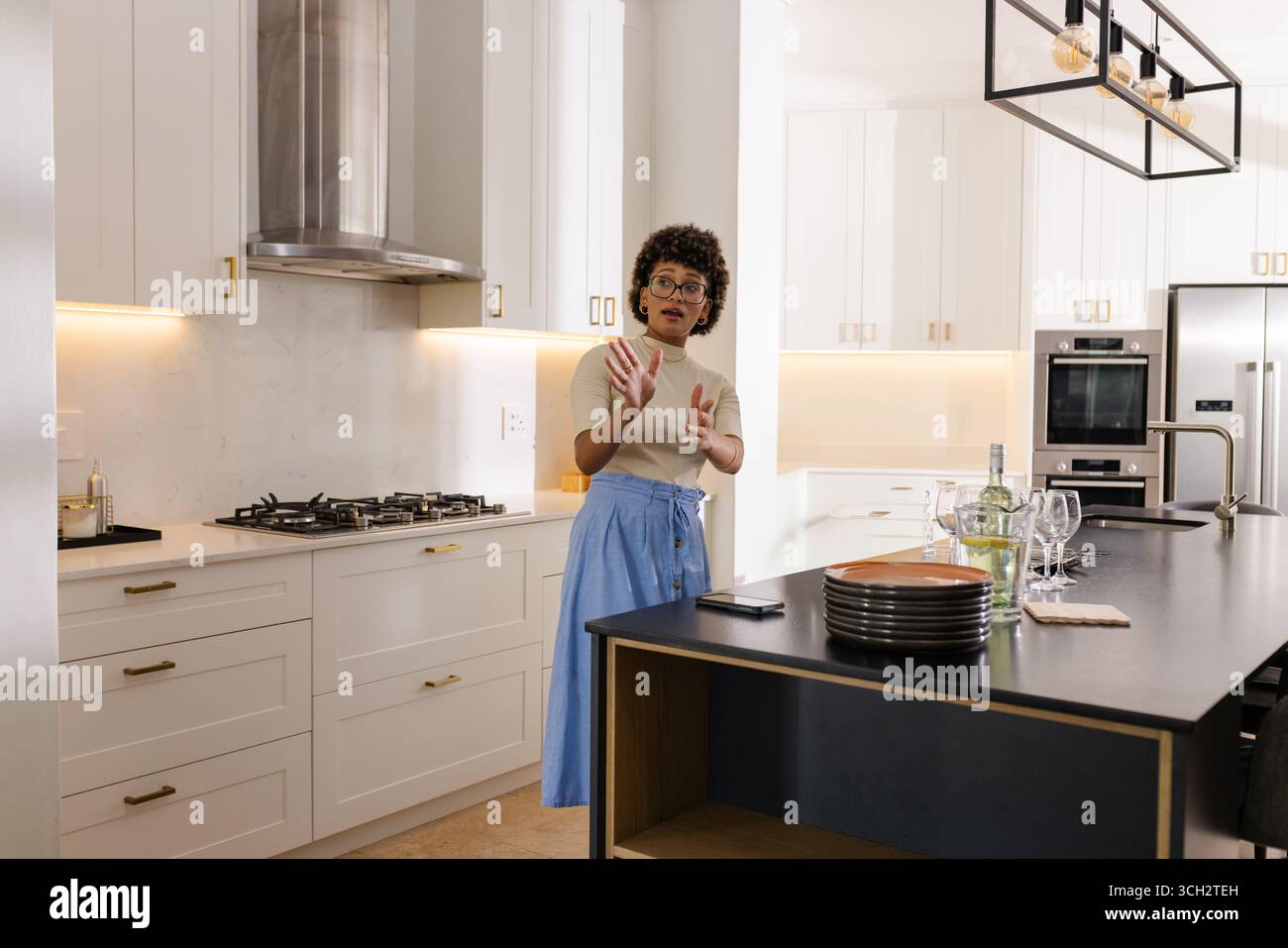 Kücheninsel mit mattschwarzer Arbeitsplatte mit gestapelten Tellern, Weingläsern, Flasche, Telefon Stockfoto