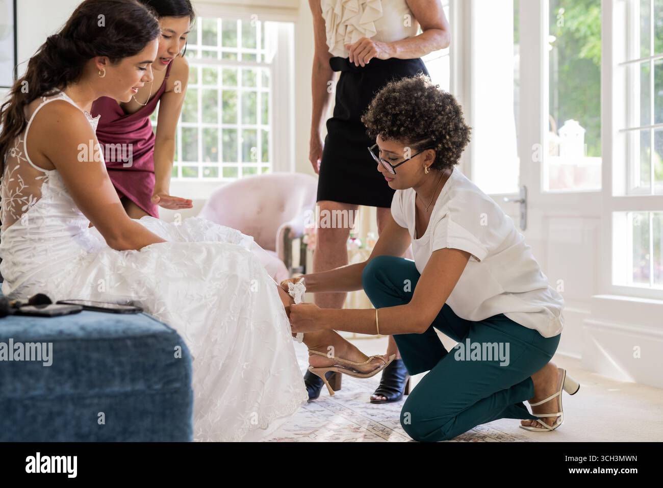 Braut bereitet sich mit Freunden vor, passt Kleid und Schuhe in einem eleganten Zimmer an Stockfoto