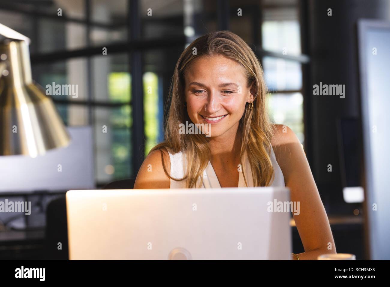 Lächelnde Frau, die im Büro am Laptop arbeitet und produktiven Abend genießt Stockfoto