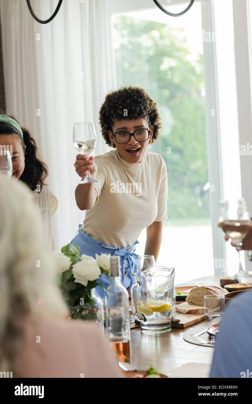 Bei einem kleinen zwanglosen Hochzeitsempfang hebt die Frau ein Glas in Toast, feiert mit Freunden zu Hause Stockfoto