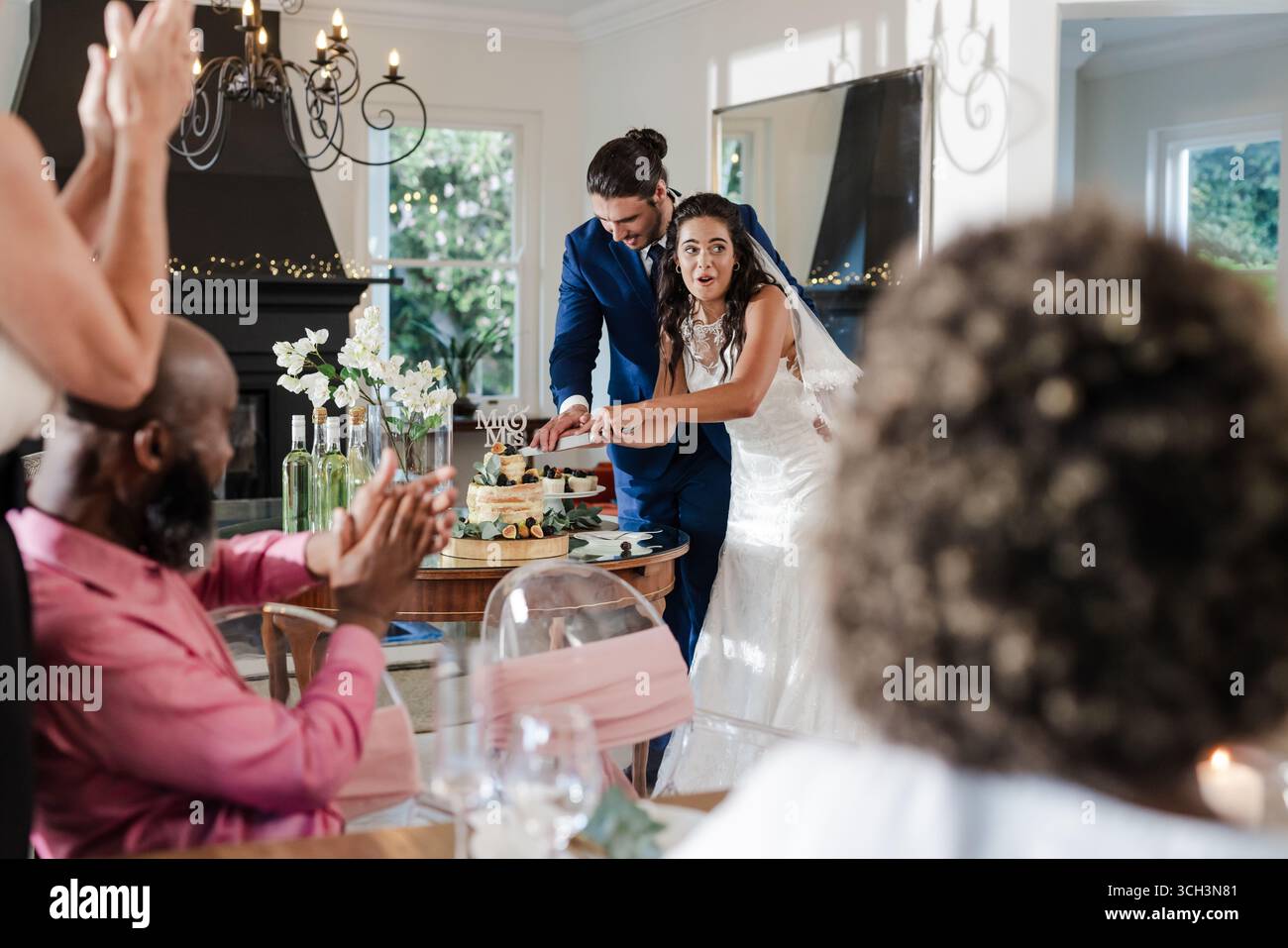 Braut und Bräutigam schneiden Hochzeitstorte, während die Gäste applaudieren Stockfoto