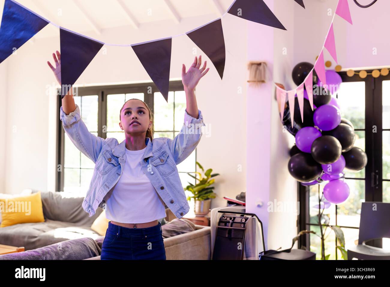 Junge Frau hängte Banner im Wohnzimmer auf, mit Ballons und Pflanzen, bereitete Partydekorationen vor Stockfoto