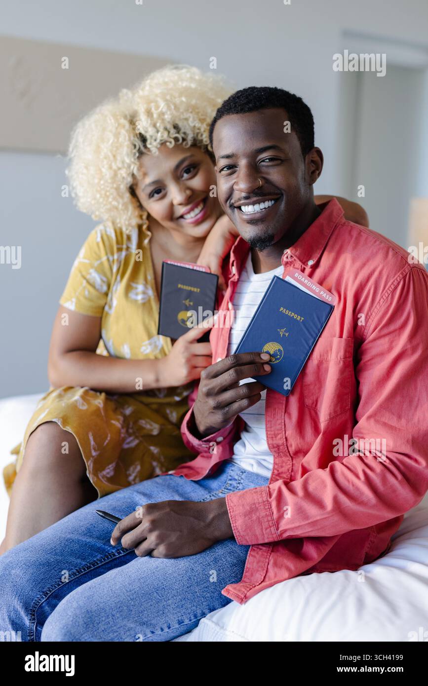 Glückliches afroamerikanisches afroamerikanisches Paar mit Pässen, auf dem Bett sitzend, bereit für die Reise Stockfoto