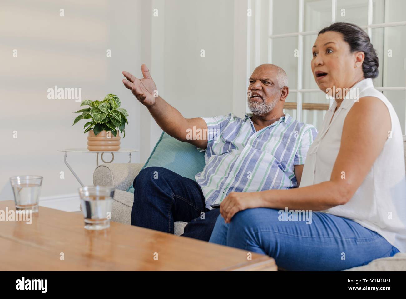 Zuhause Fernsehen, ein älteres Paar, das auf dem Sofa saß und überraschte Stockfoto