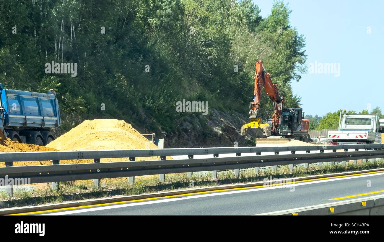Autobahnbaustelle mit Baggern und Lkw, die in der Nähe von Lärmschutzbarrieren und Waldgebieten arbeiten. Dresden, Deutschland - 19. August 2025 Stockfoto