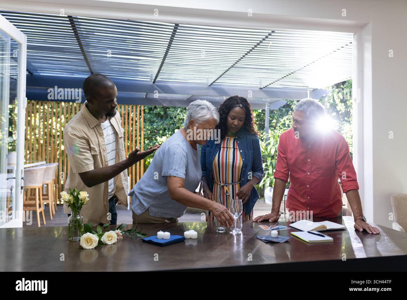 Familie zu Hause, drei Generationen bereiten Tisch mit Blumen und Gläsern vor Stockfoto