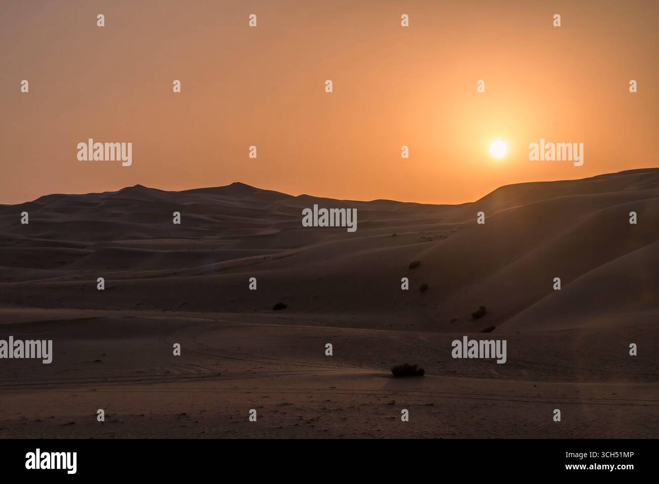 VAE - Abu Dhabi - Liwa-Wüste - Sonnenuntergang mit weitläufigen Dünen und schattigen Bergketten unter trübem Himmel Stockfoto