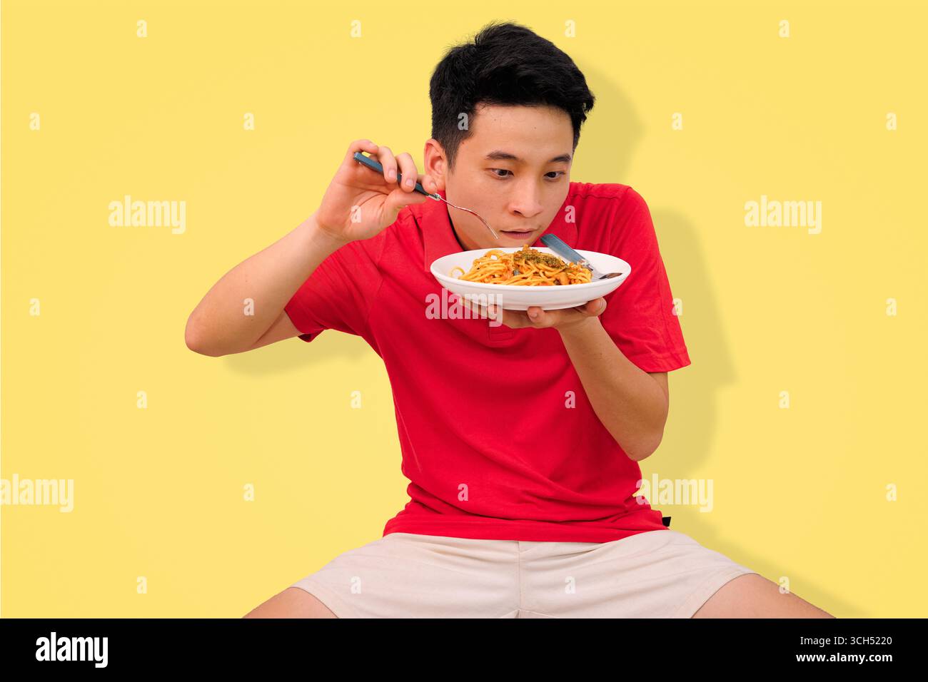 Mann genießt Spaghetti-Mahlzeit mit fröhlichem Ausdruck auf hellgelbem Hintergrund Stockfoto