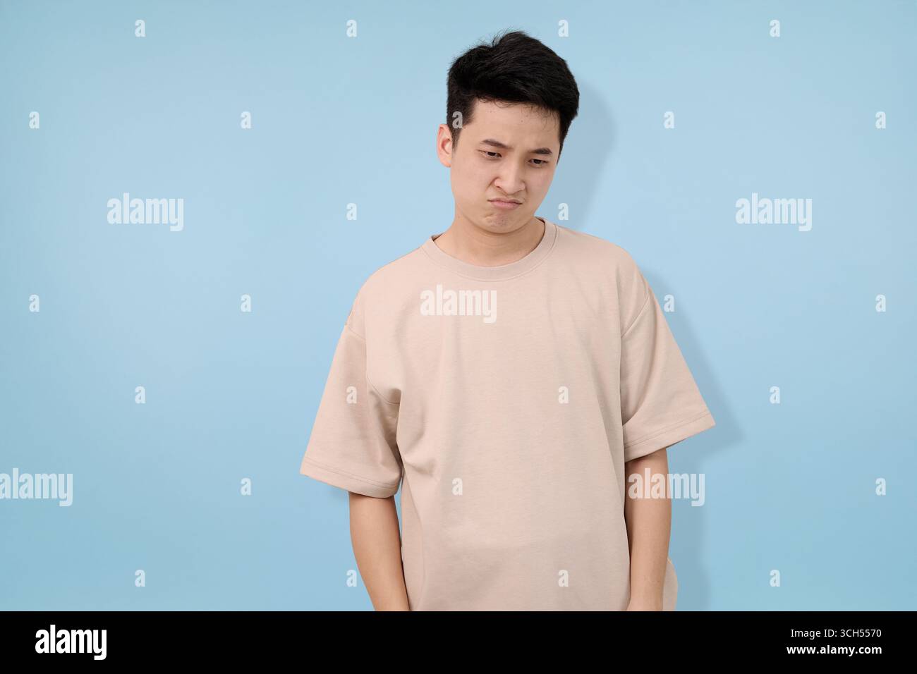 Mann, der sich vor blauem Hintergrund enttäuscht fühlt, in lässigem beigem T-Shirt Stockfoto