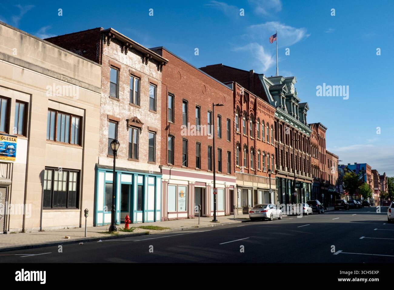 Holyoke, MA - USA - 24. August 2025 Eine Reihe historischer Backsteinfassaden säumt eine ruhige Straße in der Innenstadt von Holyoke, gekrönt von kunstvollen Fassaden und einem Ameri Stockfoto
