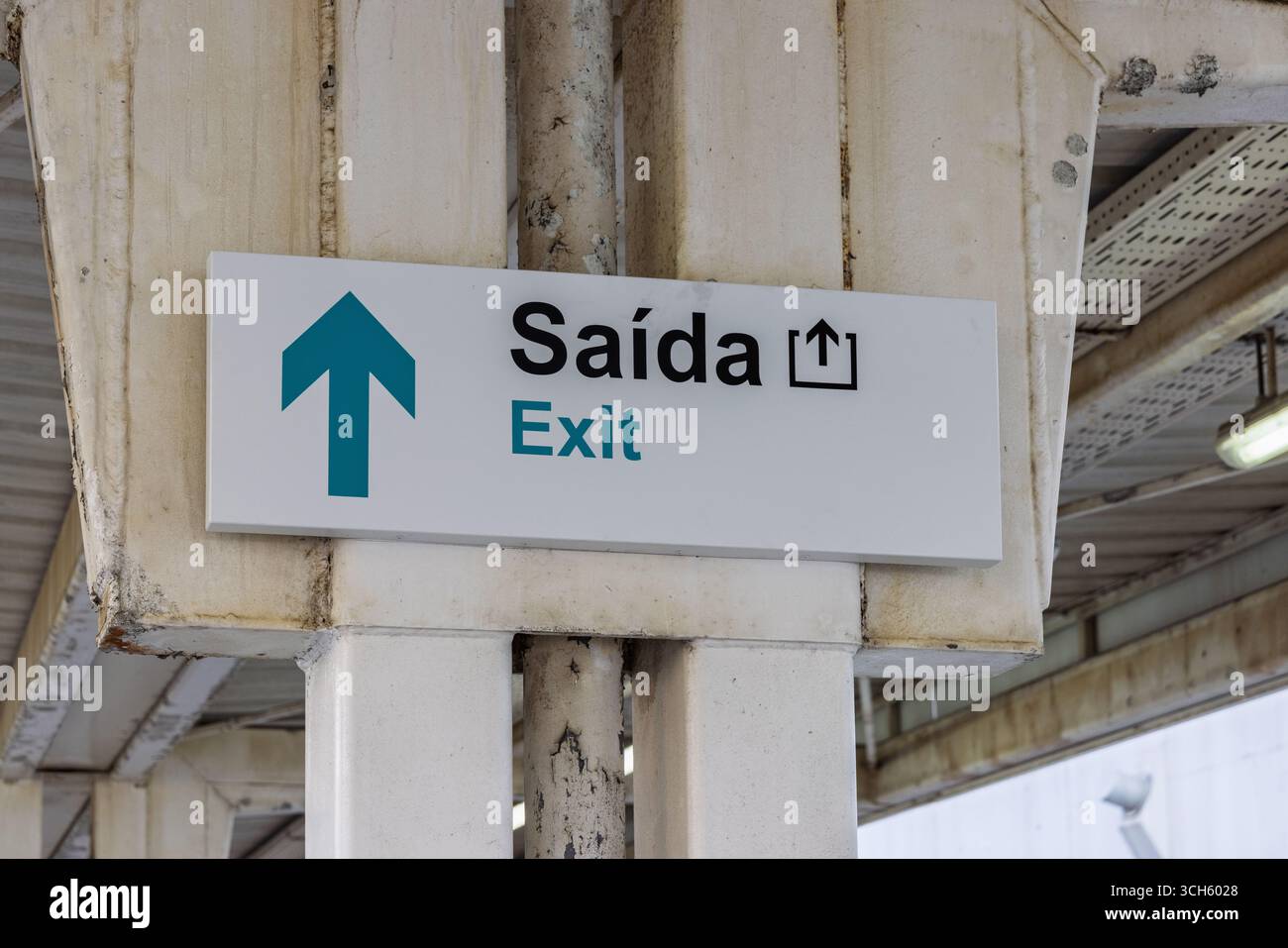 Ausstiegsschild an einem portugiesischen Bahnhof mit zweisprachigem Text „Saída / Exit“, montiert auf einer Betonsäule unter einer verwitterten Dachkonstruktion. Stockfoto