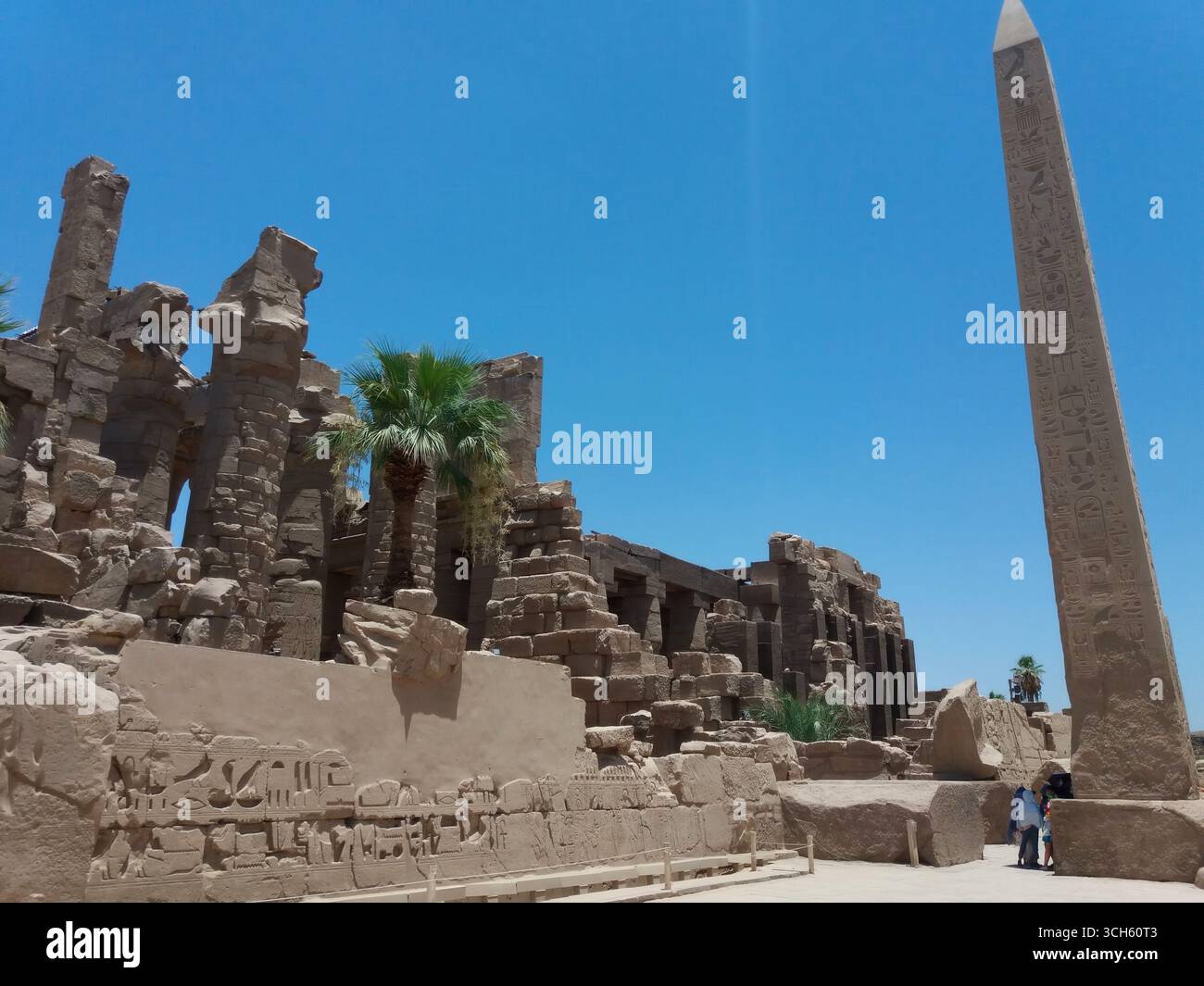 Besucher bewundern den hoch aufragenden Obelisken und die kunstvoll geschnitzten Steinstrukturen im Karnak-Tempel in Luxor, Ägypten, einer Stätte, die reich an alter Geschichte und Kult ist Stockfoto