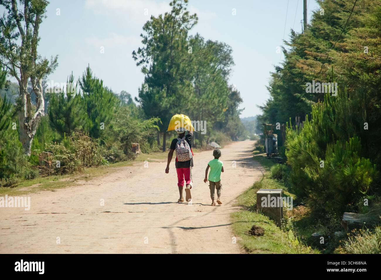 Madagaskar. 25. Oktober 2023. Typische Landschaft Madagaskars. Leute in hellen Kleidern, die die Straße entlang laufen. Frauen mit schwerer Kopfbelastung, Korb Stockfoto