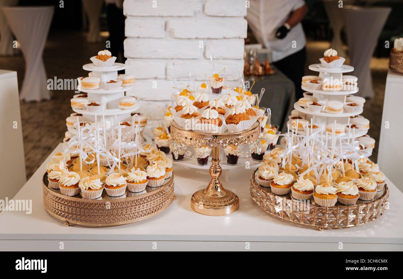 Luxuriöse Schokoriegel mit Cupcakes, Macarons und Desserts auf eleganten goldenen Tabletts Stockfoto