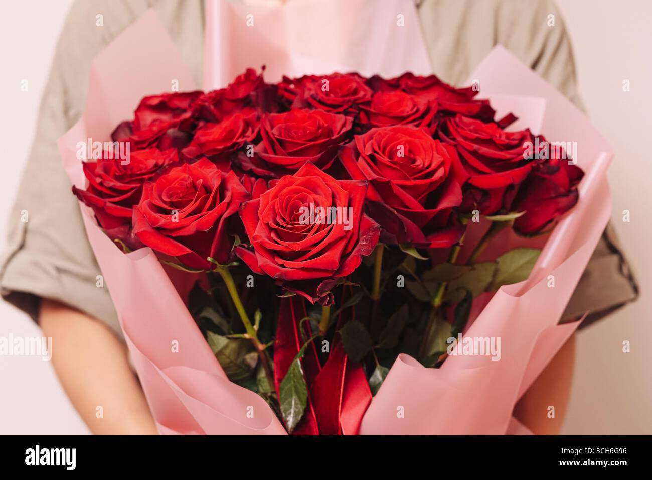 Wunderschöner Strauß aus roten Rosen in Papierfolie. Romantisches Blumengeschenk. Frische Blumen in den Händen. Natürliches Symbol für Liebe und Feier. Stockfoto