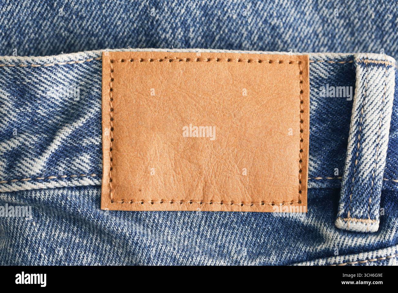 Jeansstoff mit Lederetikett in Nahaufnahme. Hintergrund mit Denim-Textur. Modische Kleidung mit braunem Patch. Modernes Textilindustriekonzept. Stockfoto