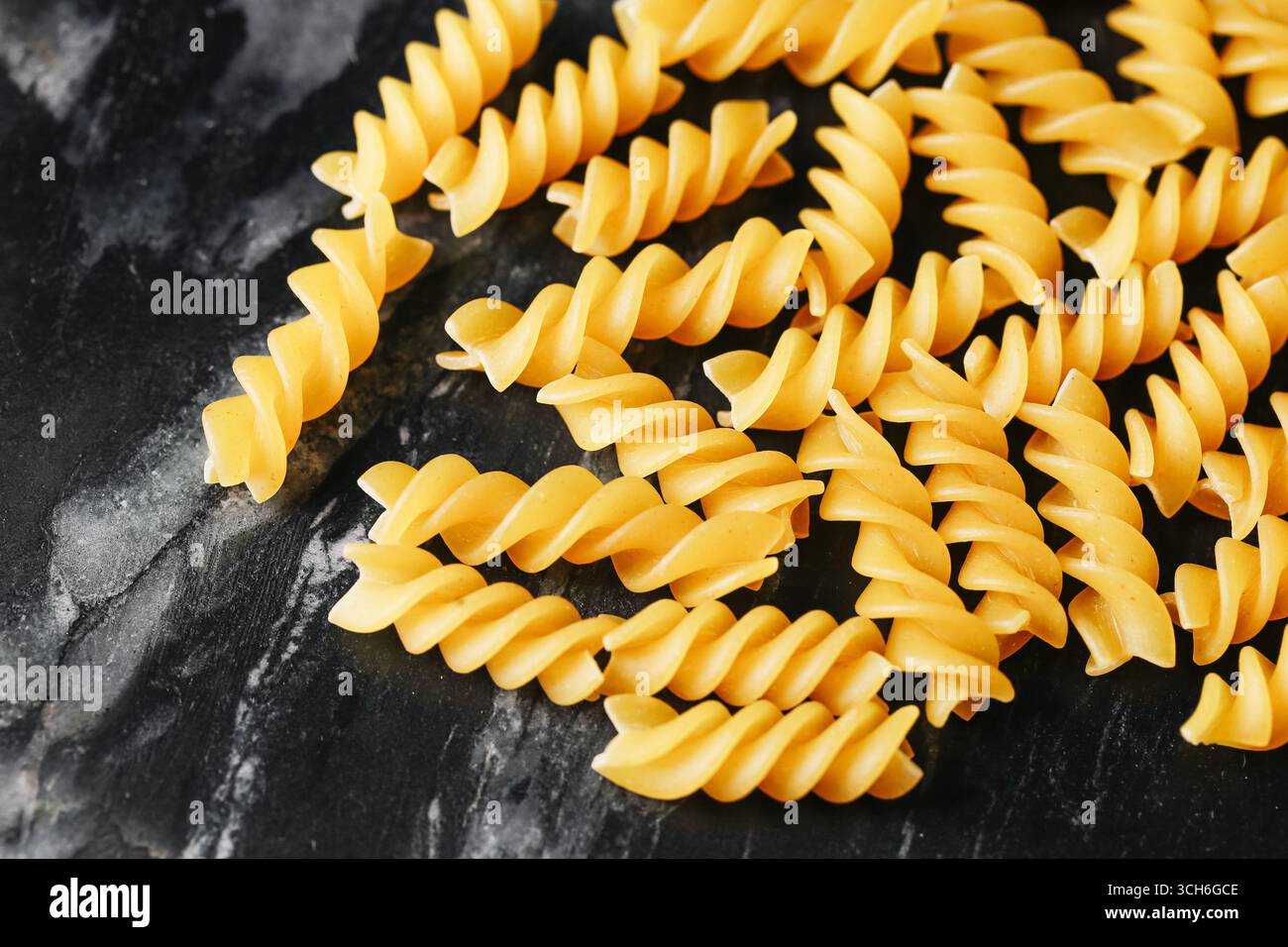 Gelbe Fusilli-Pasta auf schwarzer Marmoroberfläche. Spiral-Makkaroni-Hintergrund. Italienische Lebensmittelzutat zum Kochen. Traditionelle trockene Nudeln Nahaufnahme. Stockfoto