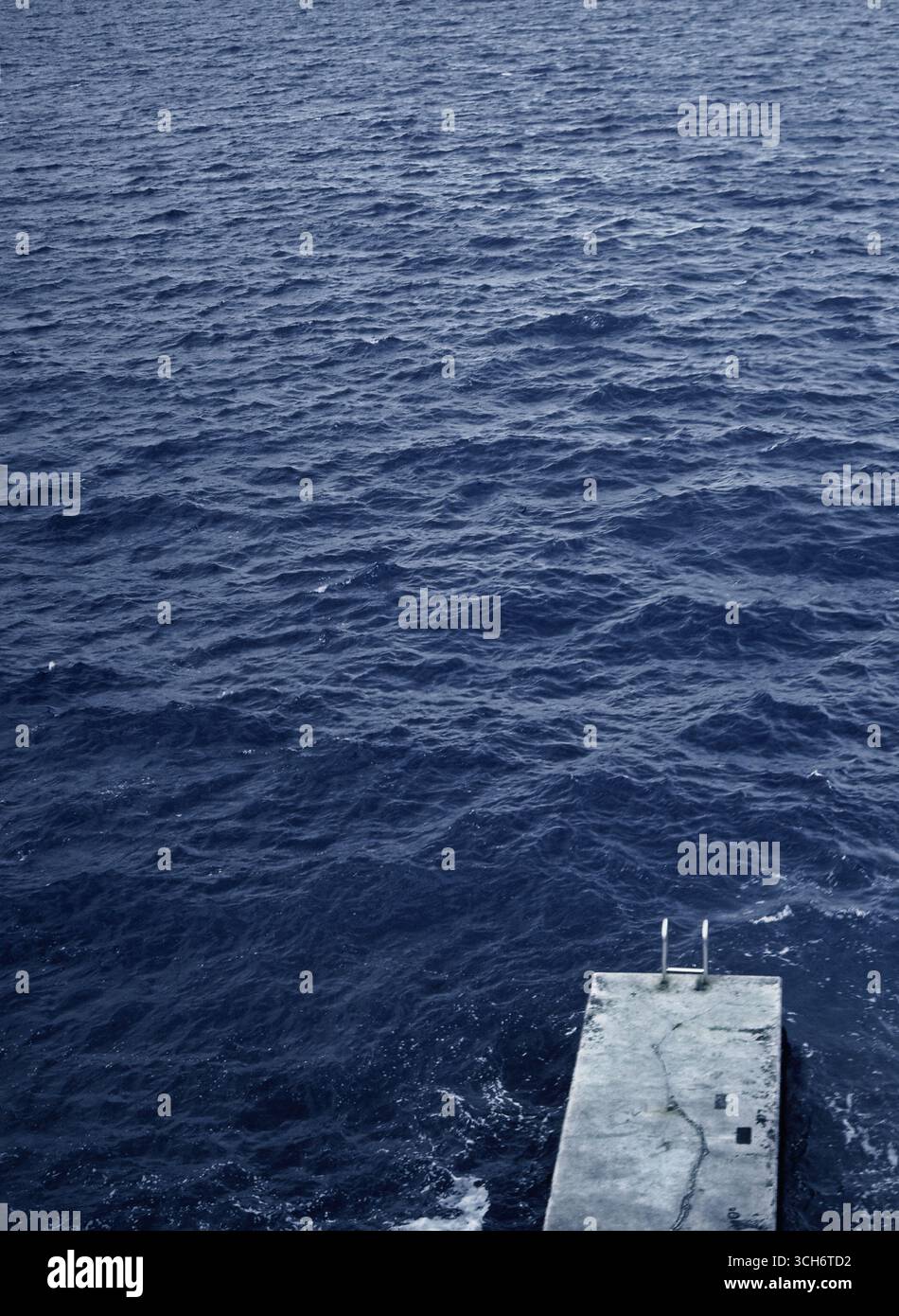 Hochwinkelaufnahme eines Betonpiers mit Treppen, die in ein kaltes blaues Meer hinabführen, aufgenommen auf Mittelformat-Slidefilm ohne anwesende Personen. Stockfoto