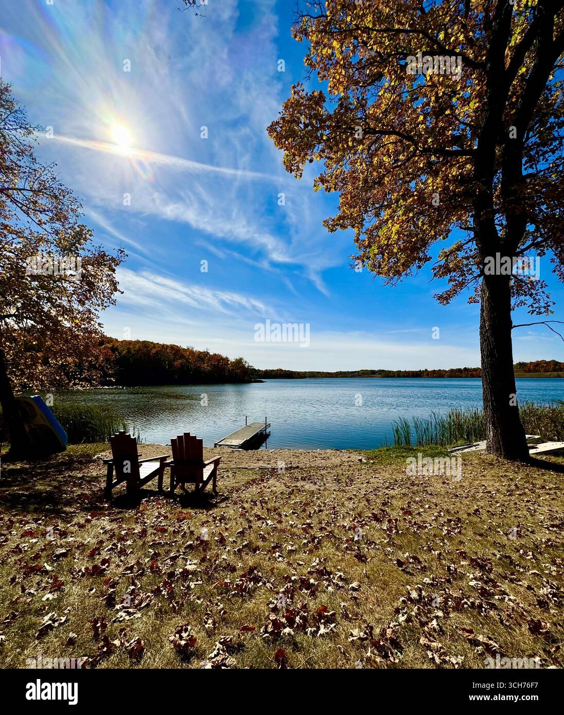 Der See selbst ist ein ruhiger Spiegel, der das feurige Schauspiel der Baumkronen reflektiert, während sie sich anmutig zum Wasser neigen. - Smartphone-aufgenommenes Stockfoto