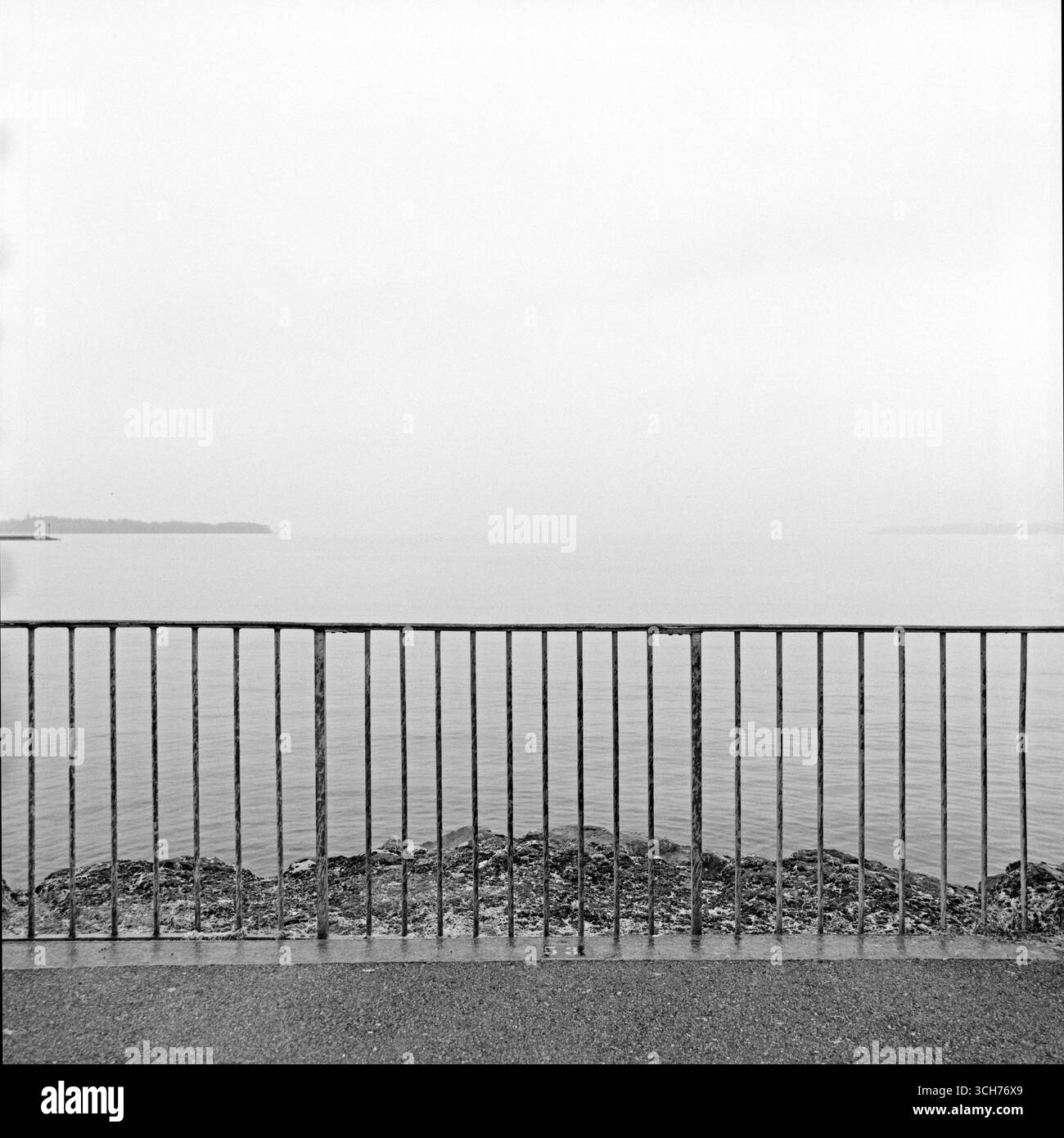 Die Atmosphäre ist ruhig und minimal, der bewölkte Himmel verschmilzt mit dem Horizont und sanftes Licht reflektiert vom See. Stockfoto