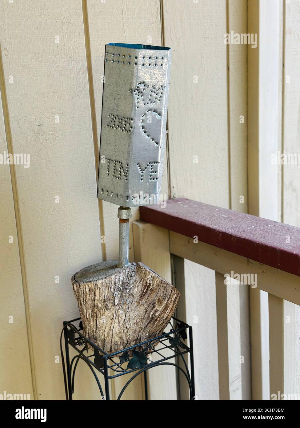 Handgefertigtes Blechkunstwerk mit perforiertem Herzdesign, montiert auf einem Holzblock und auf einem Geländer für die Veranda. - Smartphone-aufgenommenes Stockfoto