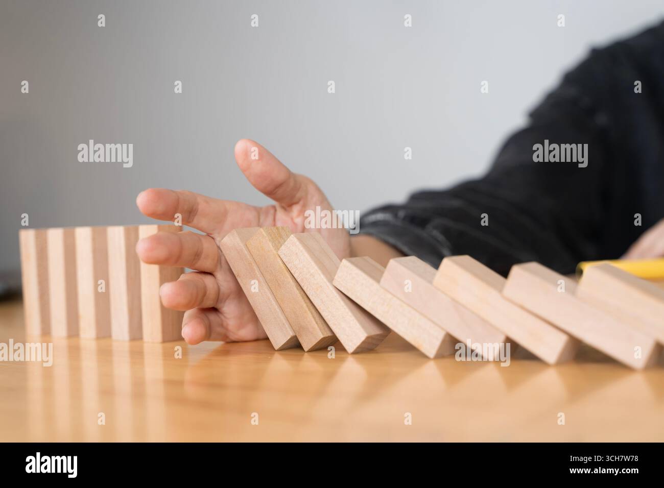 Konzept, das die Reaktion der Domino-Kette mit der Hand stoppt, um Risikomanagement, Krisenprävention, Führung, Entscheidungskontrolle, Problemlösung zu symbolisieren. ein Stockfoto