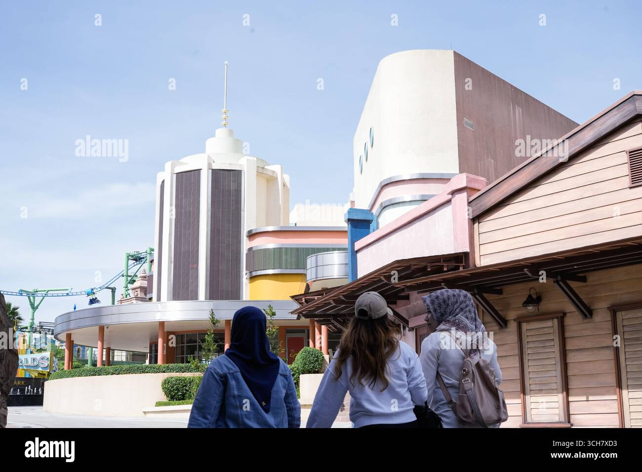 An einem geschäftigen Tag spazieren Besucher an einem sonnigen Eingang zum Freizeitpark vorbei an farbenfroher Retro-Architektur Stockfoto