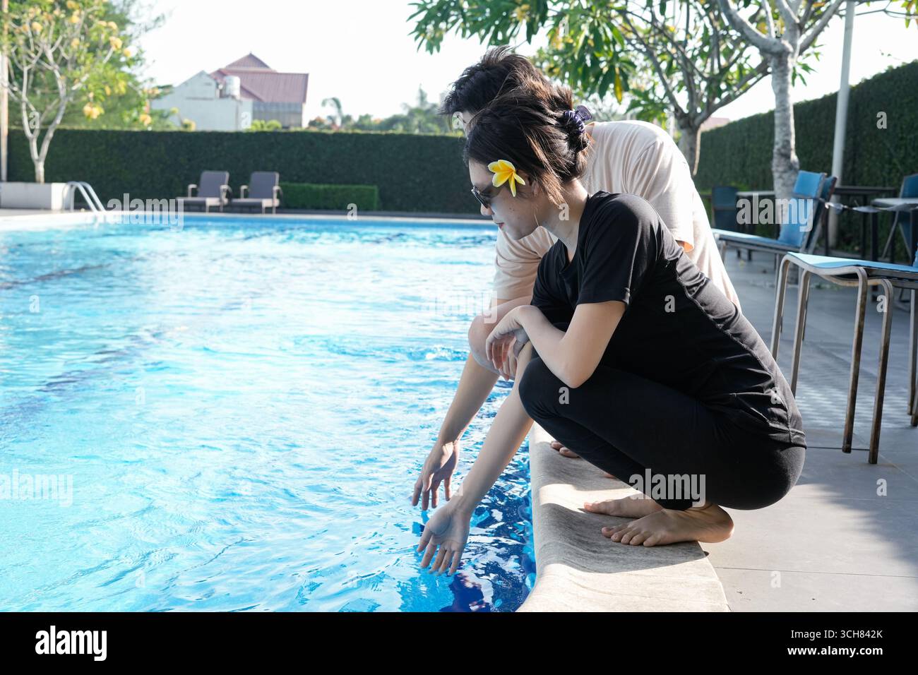 Zwei Personen, die sich neben einem lebhaften Außenpool entspannen Stockfoto