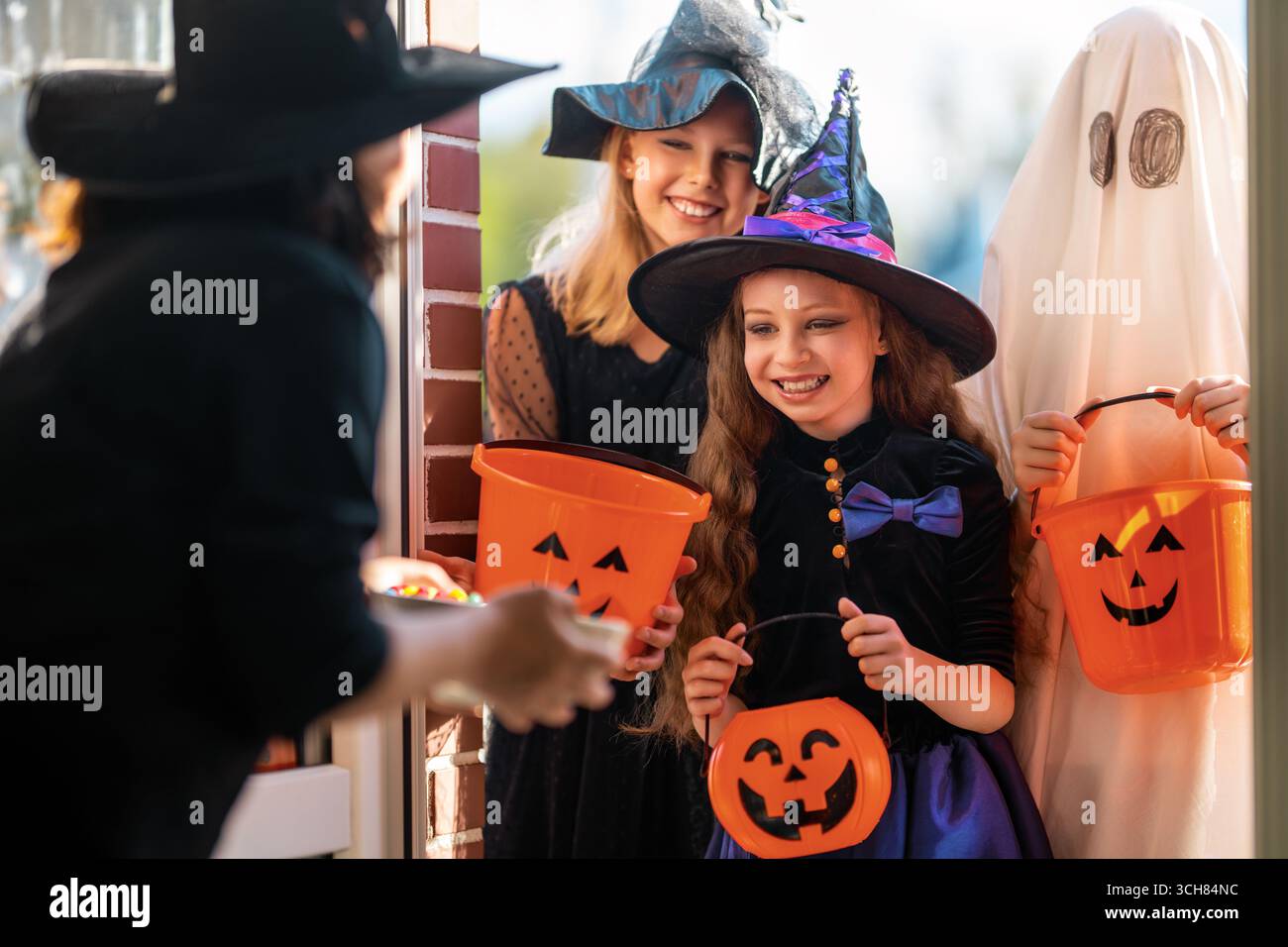 Glückliche Leute feiern Halloween. Erwachsene behandelt Kinder im Freien mit Süßigkeiten. Stockfoto