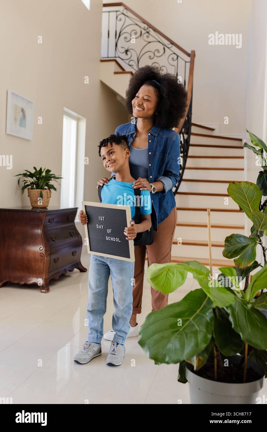 Afroamerikanische Mutter und Sohn lächeln und halten Schild für den ersten Schultag Stockfoto