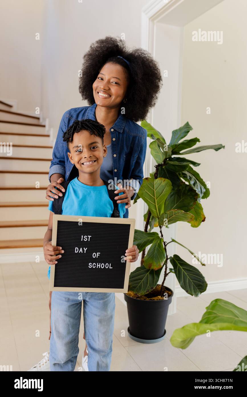Mutter und Sohn lächeln, halten das Schild für den ersten Schultag zu Hause Stockfoto