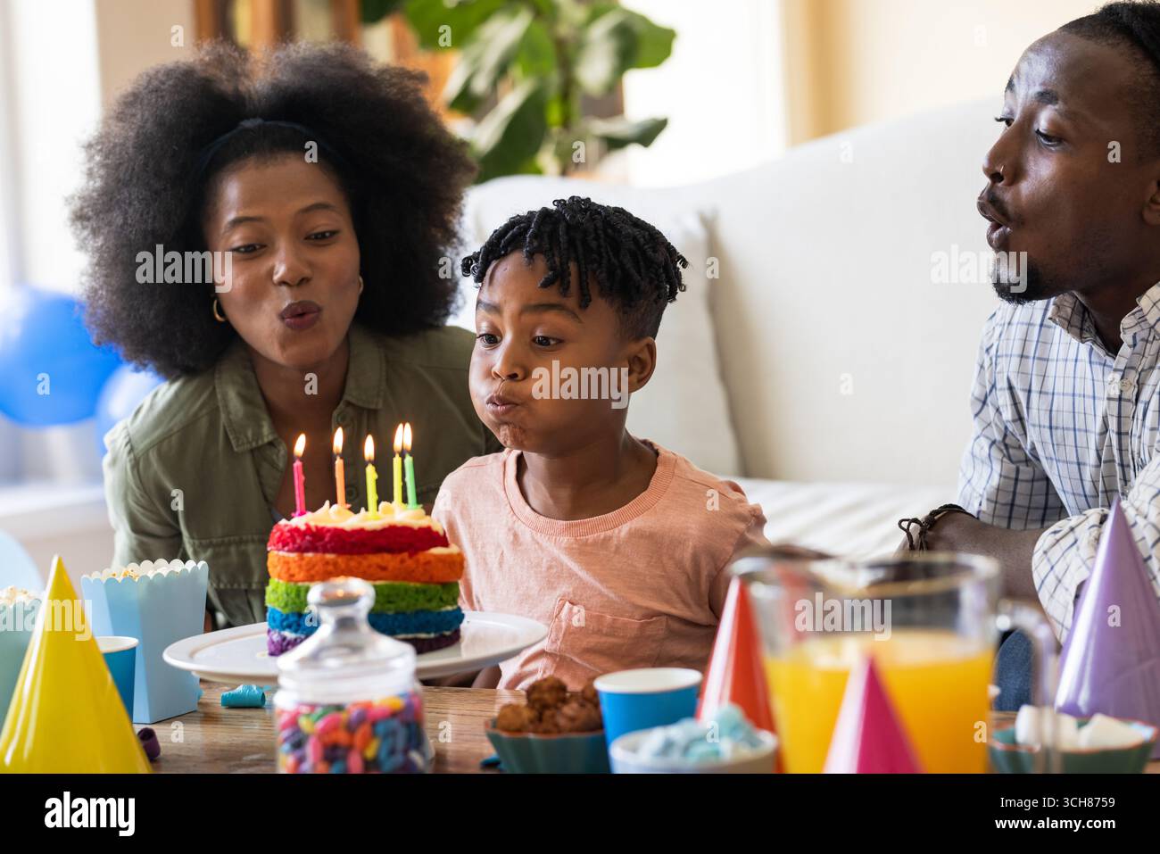 Auf der Party, bei der Geburtstagsfeier, blüht eine dreiköpfige Familie Kerzen auf buntem Kuchen zu Hause aus Stockfoto