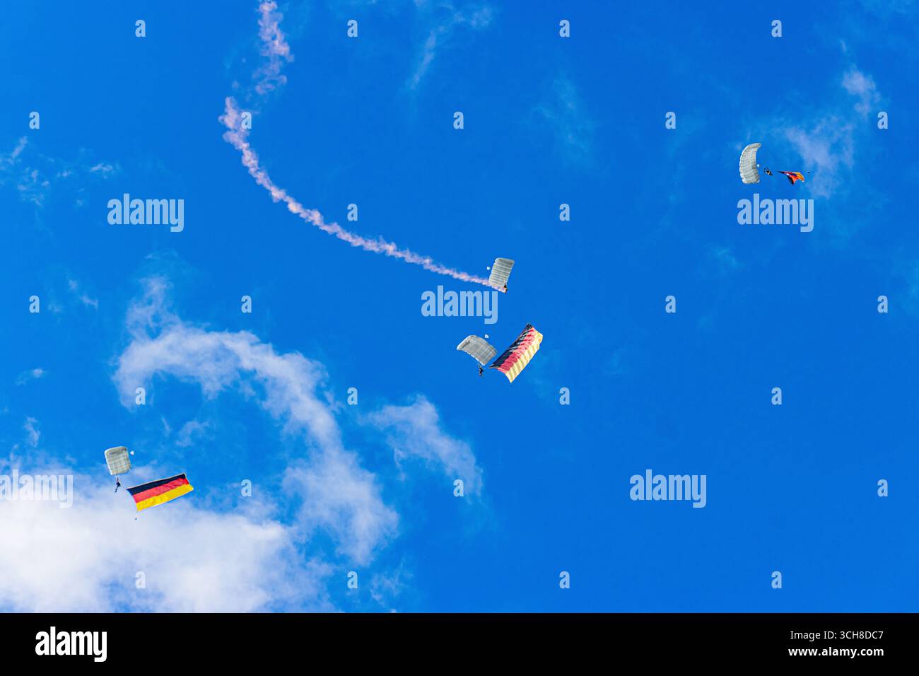 Zwei Fallschirmjäger der Bundeswehr steigen unter Fallschirmen ab, die stolz die deutsche Flagge gegen einen klaren blauen Himmel tragen, was Stärke, Einheit, A symbolisiert Stockfoto
