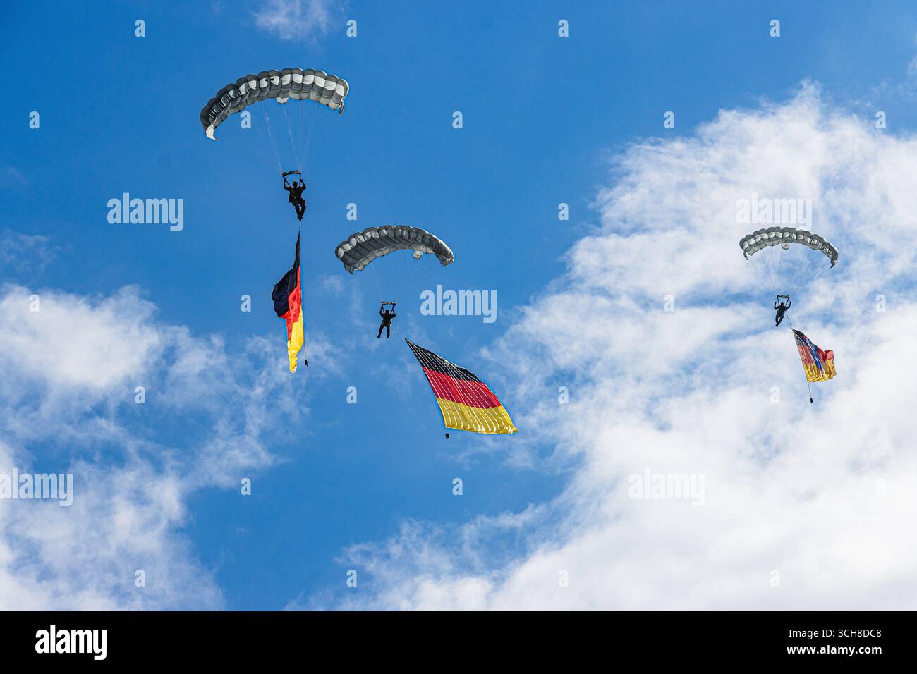 Zwei Fallschirmjäger der Bundeswehr steigen unter Fallschirmen ab, die stolz die deutsche Flagge gegen einen klaren blauen Himmel tragen, was Stärke, Einheit, A symbolisiert Stockfoto