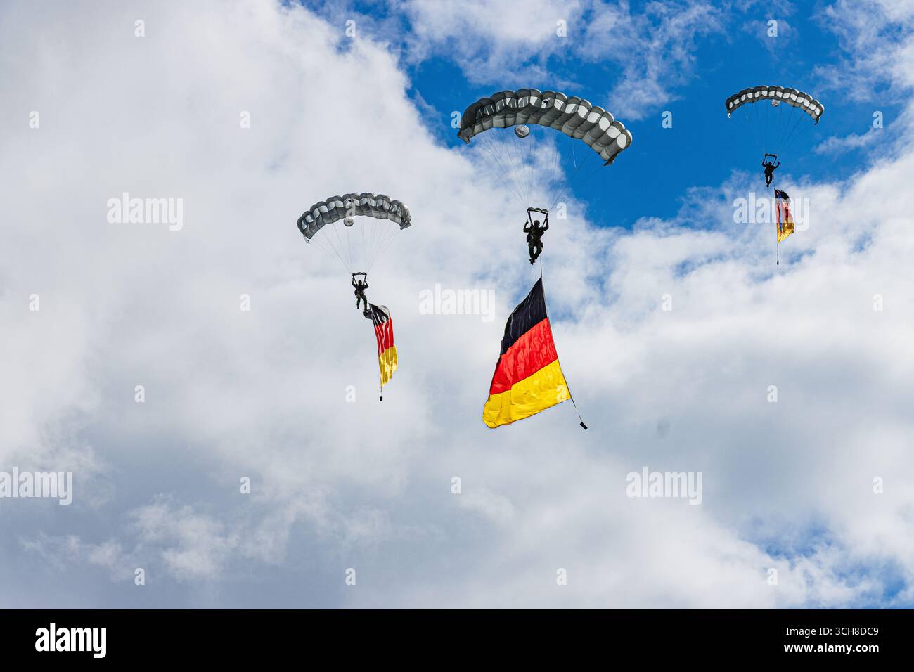 Zwei Fallschirmjäger der Bundeswehr steigen unter Fallschirmen ab, die stolz die deutsche Flagge gegen einen klaren blauen Himmel tragen, was Stärke, Einheit, A symbolisiert Stockfoto