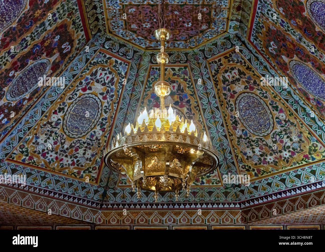 Reich verzierter Empfangsraum mit gemalter Zedernholzdecke, Kronleuchter und gekacheltem Kamin im Bahia Palace (Palais Bahia), Marrakesch, Marokko. Stockfoto