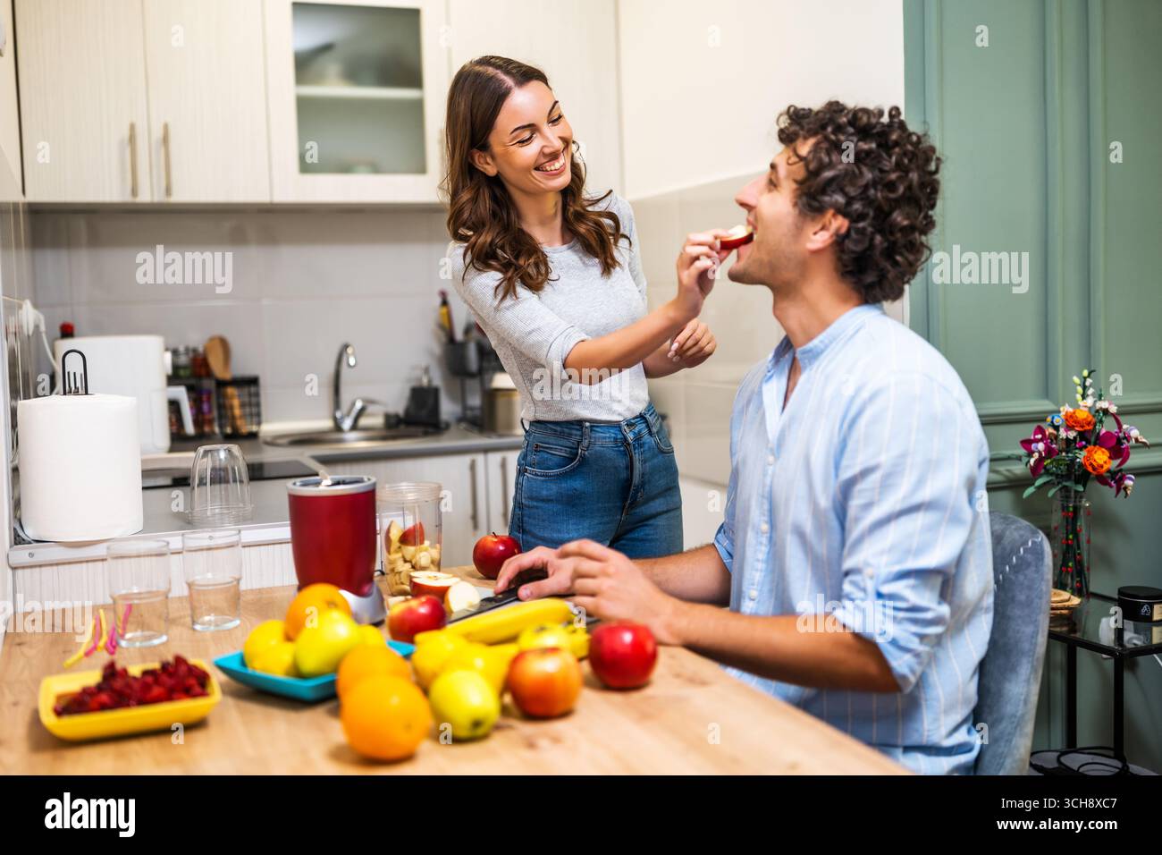 Junge Paare teilen einen Spaß beim Kochen und bereiten gesunde Frucht-Smoothies mit einem elektrischen Mixer zu. Stockfoto