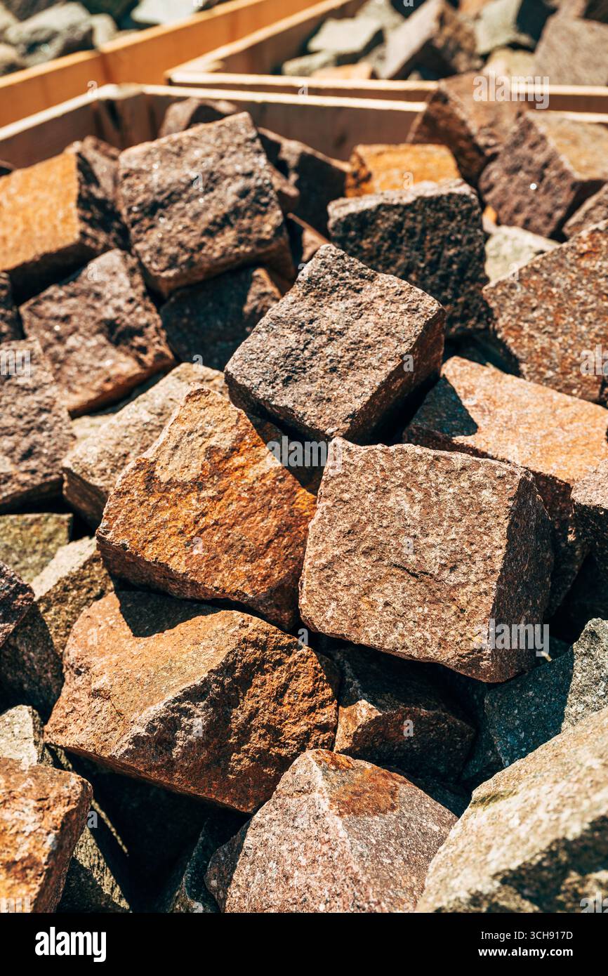 Steinwürfel aus natürlichem Porphyrstein zum Pflastern, verschiedene Erdtöne und raue Texturen im Sonnenlicht, Hintergrund aus Baumaterial. Selektiver Fokus Stockfoto