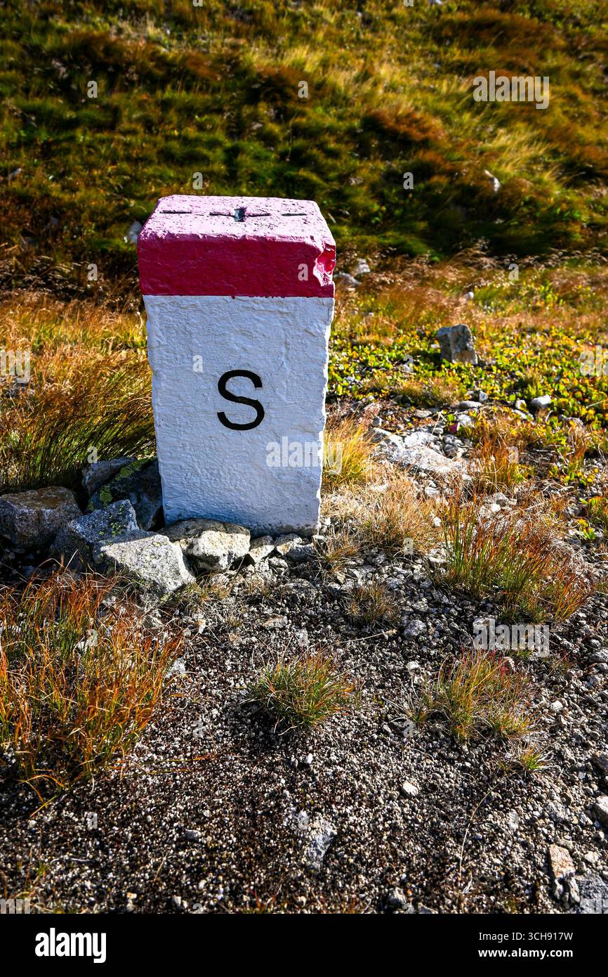 Weißer und roter Betongrenzposten, der eine Grenze zwischen zwei Ländern markiert und in einer bergigen Landschaft steht. Stockfoto