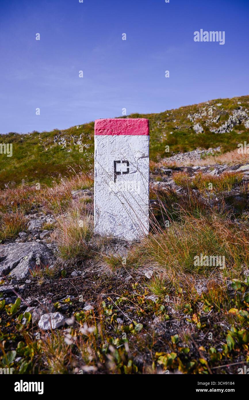 Weiße und rote Grenzmarkierung auf dem grasbewachsenen Bergrücken unter klarem blauem Himmel. Stockfoto