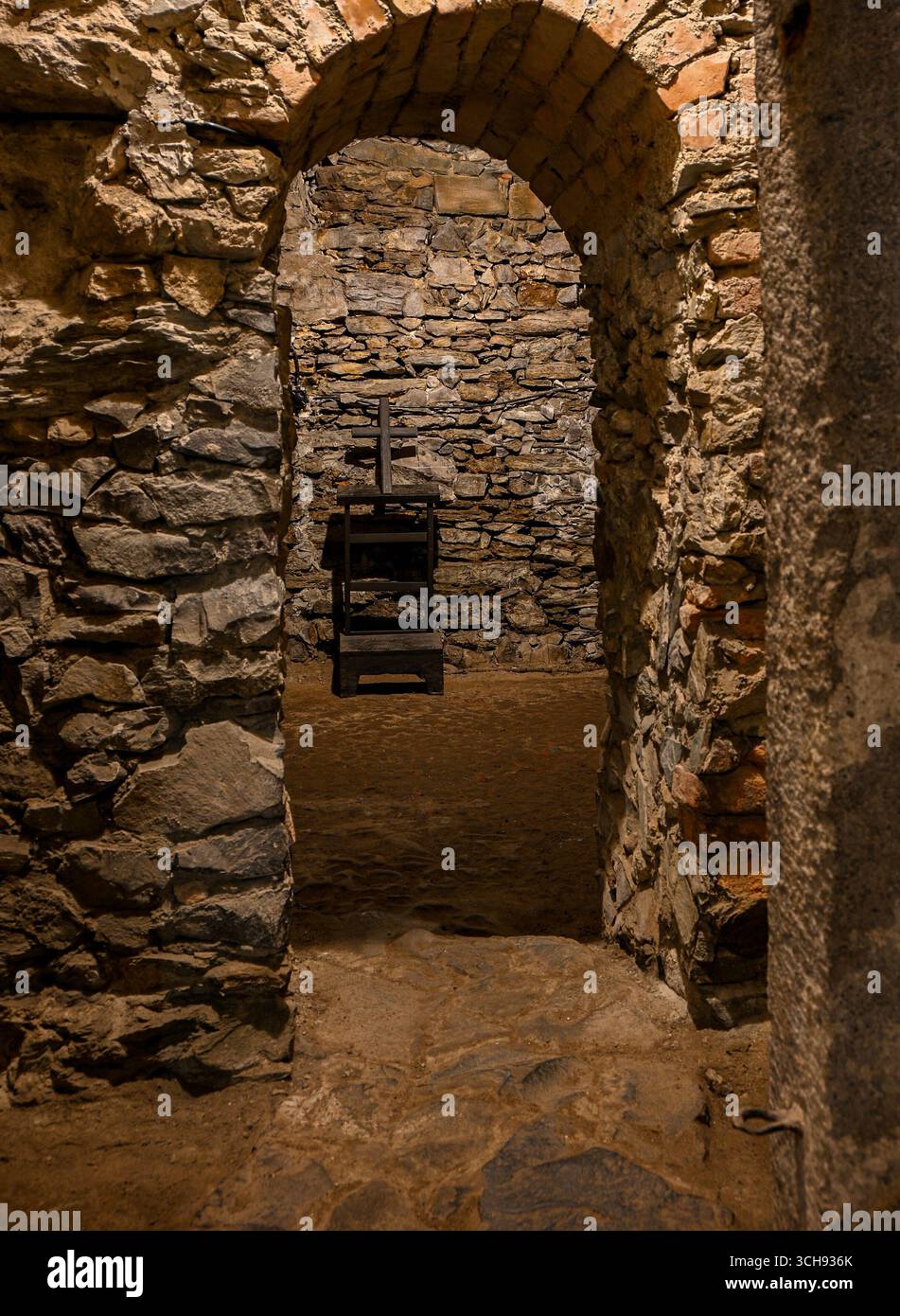 Ein Steinbogen führt in die mittelalterliche Folterkammer mit Holzkreuz und Hocker, wodurch eine unheimliche Atmosphäre entsteht. Stockfoto
