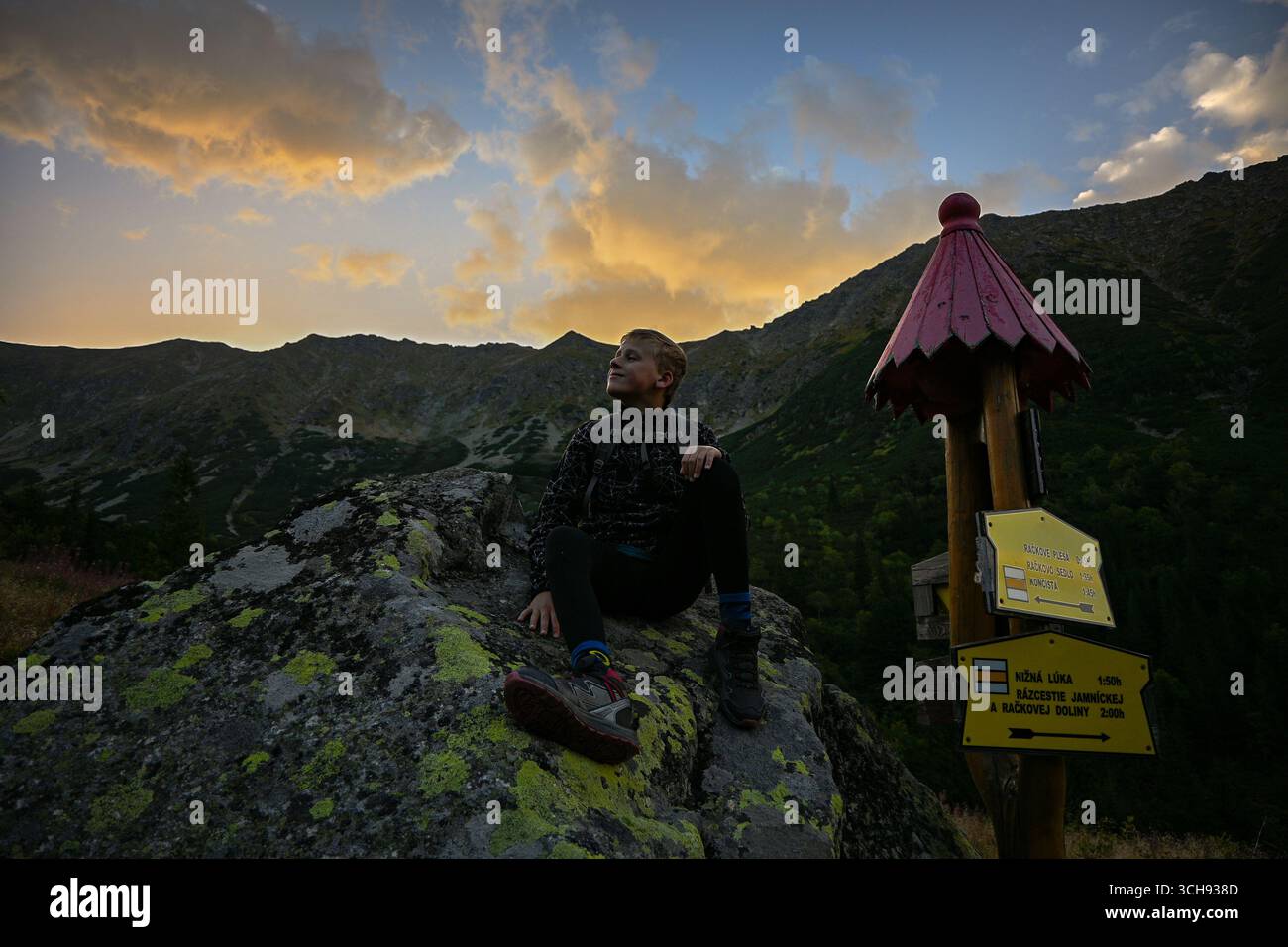 Ein Wanderer ruht auf einem Felsen und genießt einen wunderschönen Sonnenuntergang über einem Bergtal in der hohen tatra. Stockfoto