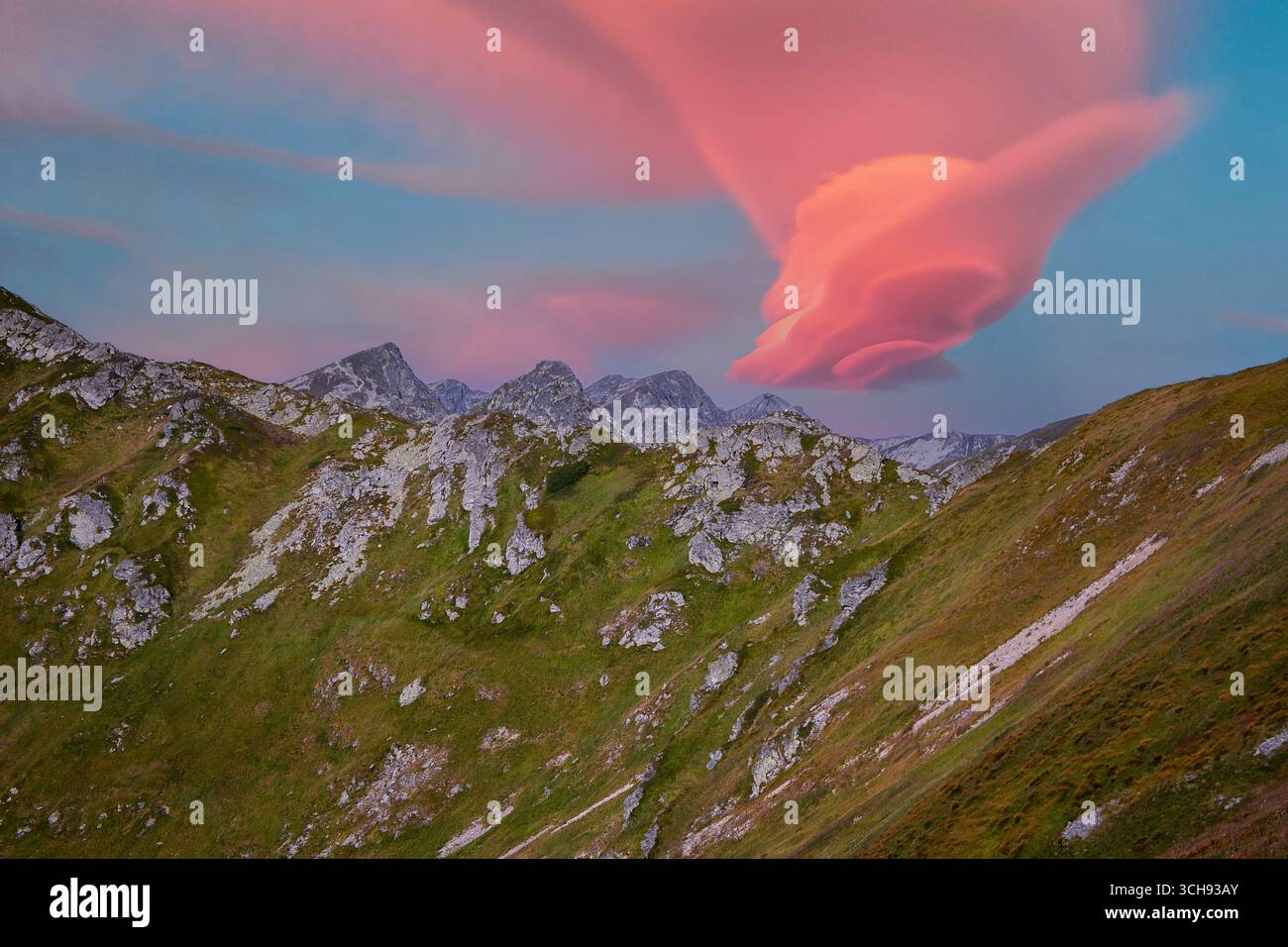 Die leuchtende Lentikularwolke beleuchtet den Himmel über einer zerklüfteten Berglandschaft bei einem atemberaubenden Sonnenuntergang. Stockfoto