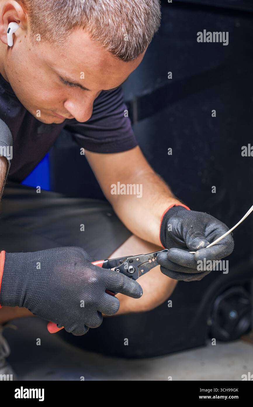 Ein Mann hält elektrische Kabel und Werkzeuge, während er ein Garagentor repariert Stockfoto