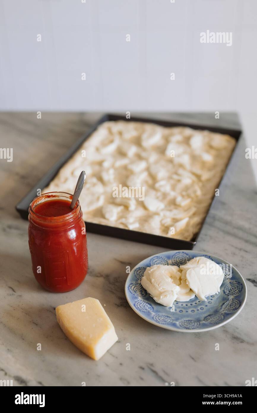 Käsegarnitur auf ungebackenem Pizzateig in Backpfanne Stockfoto