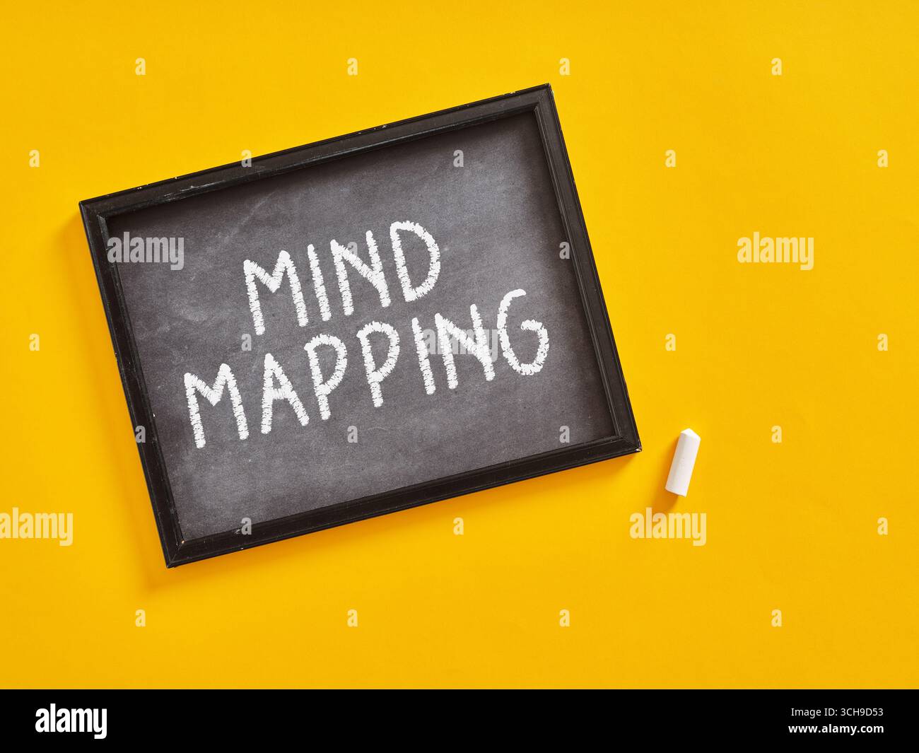 Tafel mit Mindmapping-Inschrift und einem Stück Kreide auf gelbem Hintergrund, das Brainstorming und kreativen Denkprozess darstellt Stockfoto